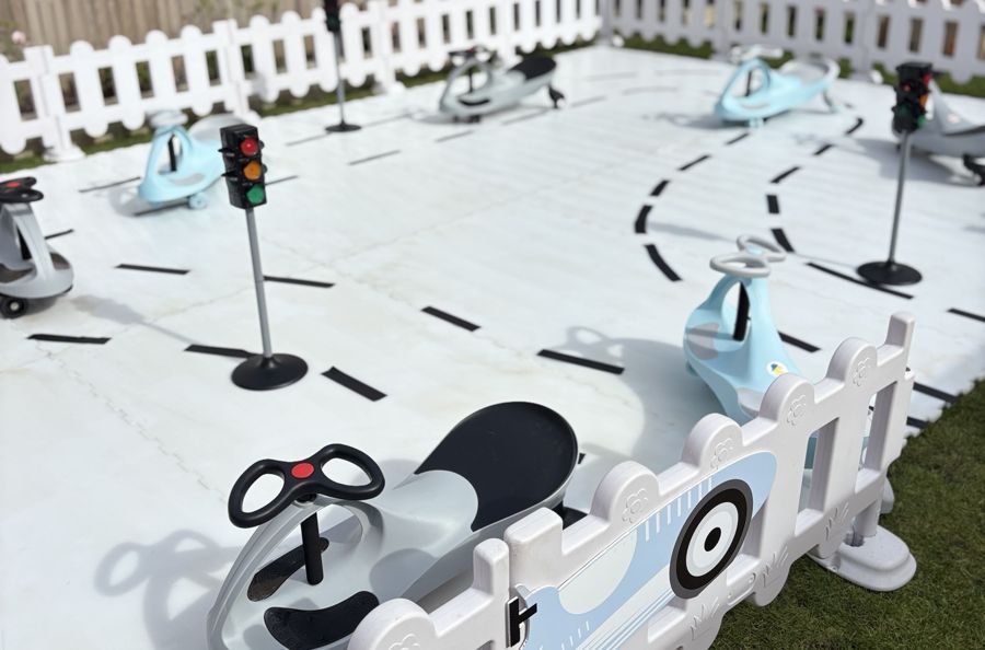 DIDI ride-on cars on a white road-marked track with traffic lights and white fencing in a garden
