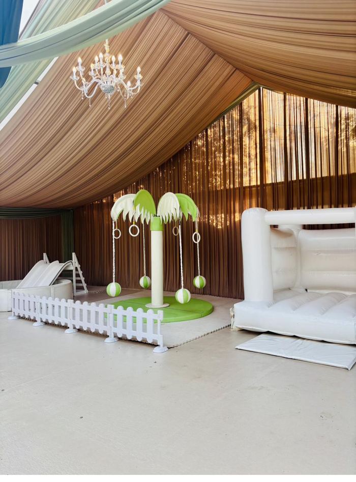 Green Carousel Tree with ball pit, slides and white bouncy castle inside a draped marquee