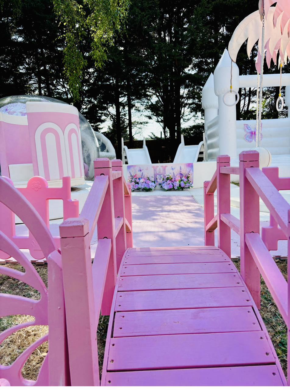 Pink bridge leading into a lilac butterfly setup with a personalised letter H sign and flowers